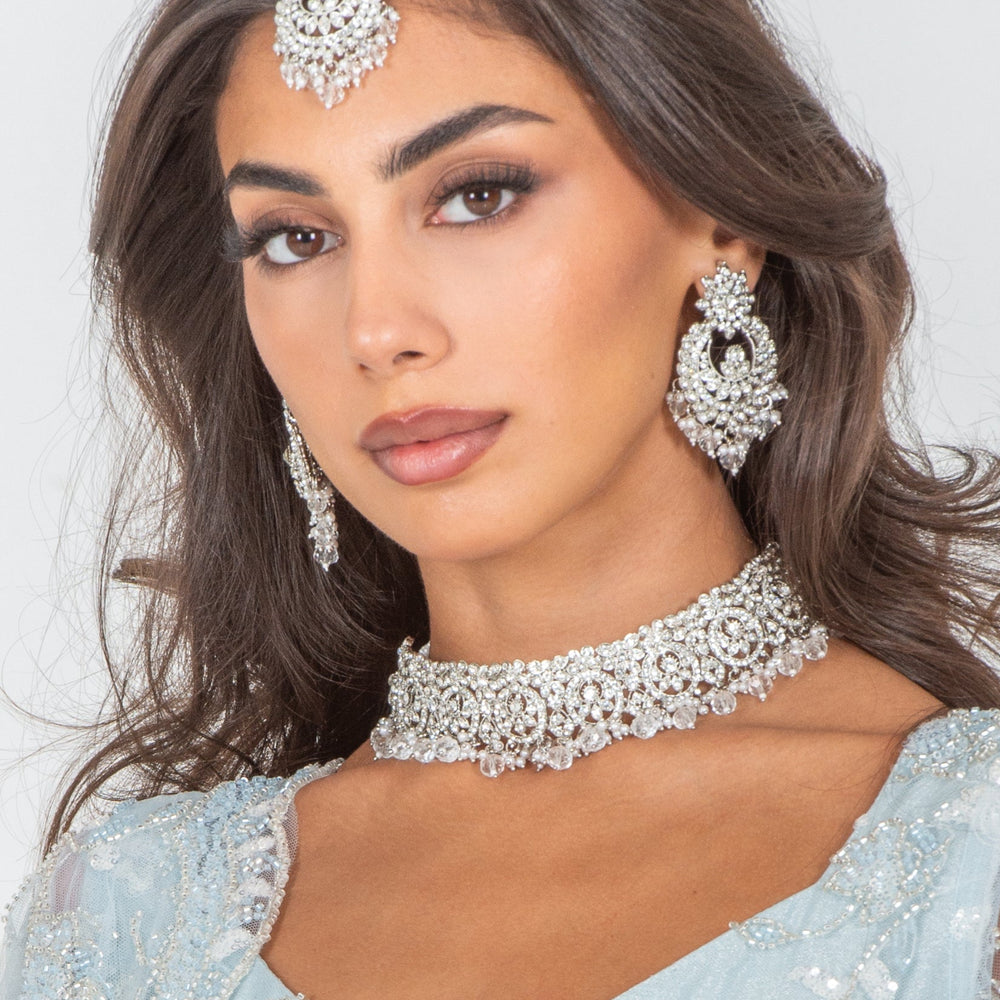 Woman wearing a light blue traditional outfit with silver jewelry against a white background