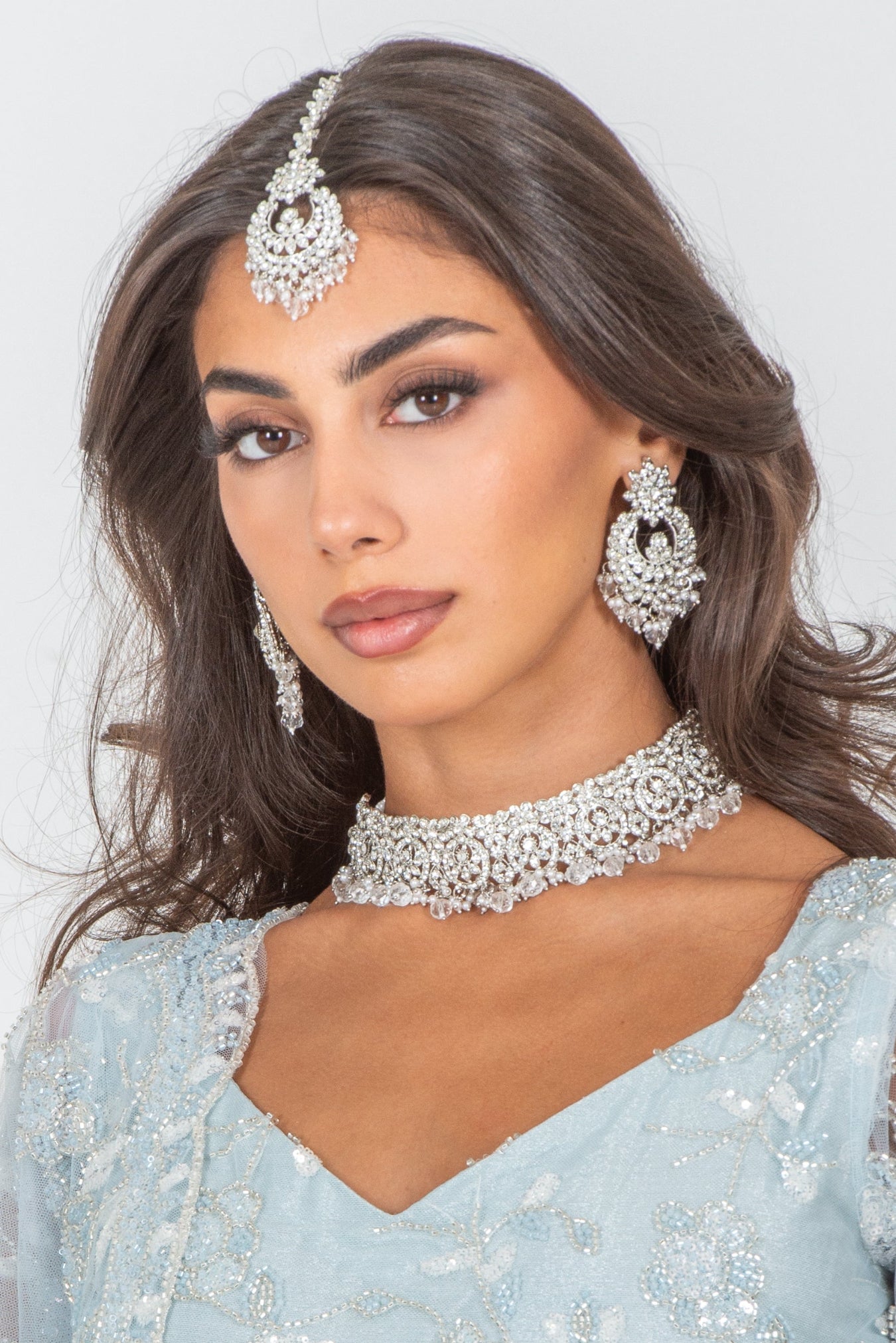Woman wearing a light blue traditional outfit with silver jewelry against a white background