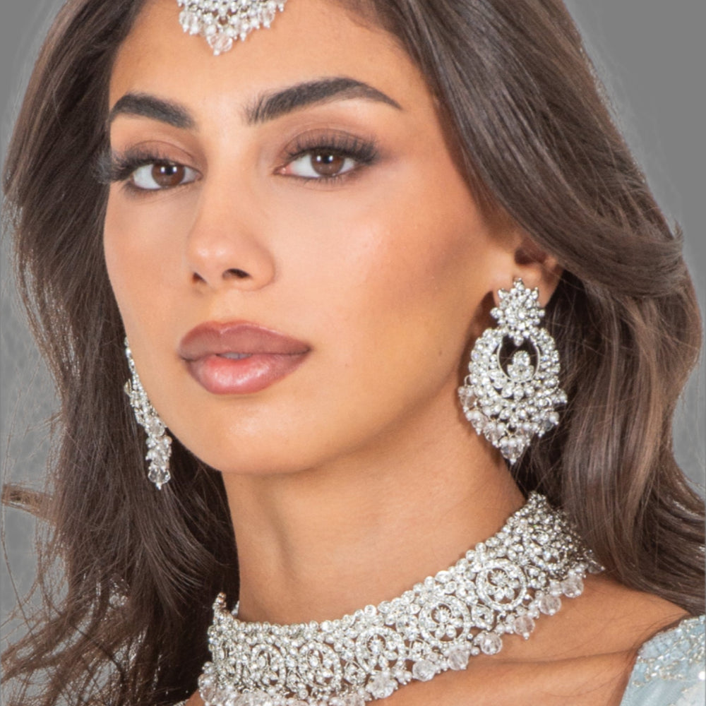 Woman wearing silver jewelry including earrings and a necklace against a white background