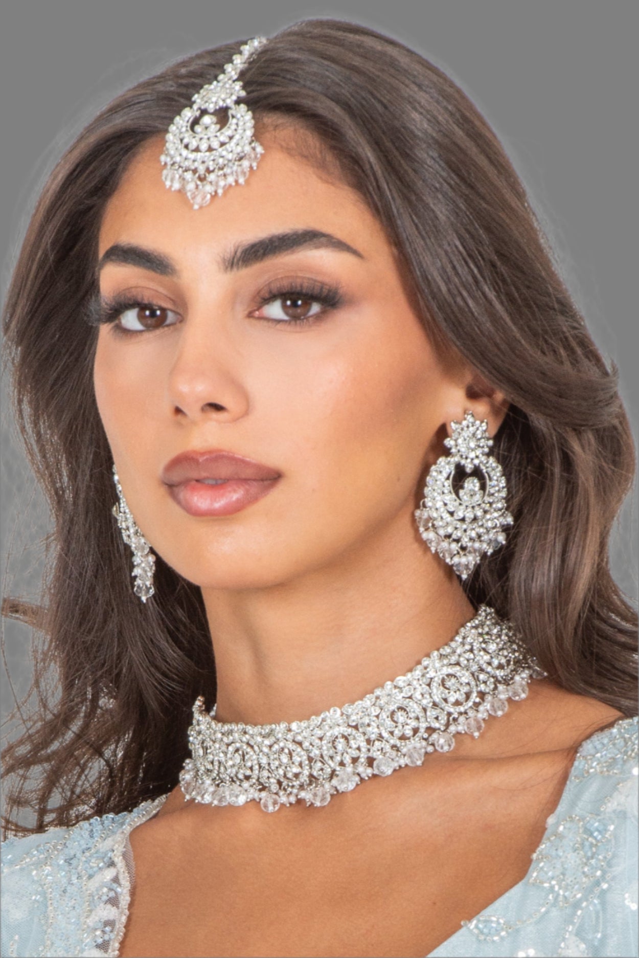 Woman wearing silver jewelry including earrings and a necklace against a white background