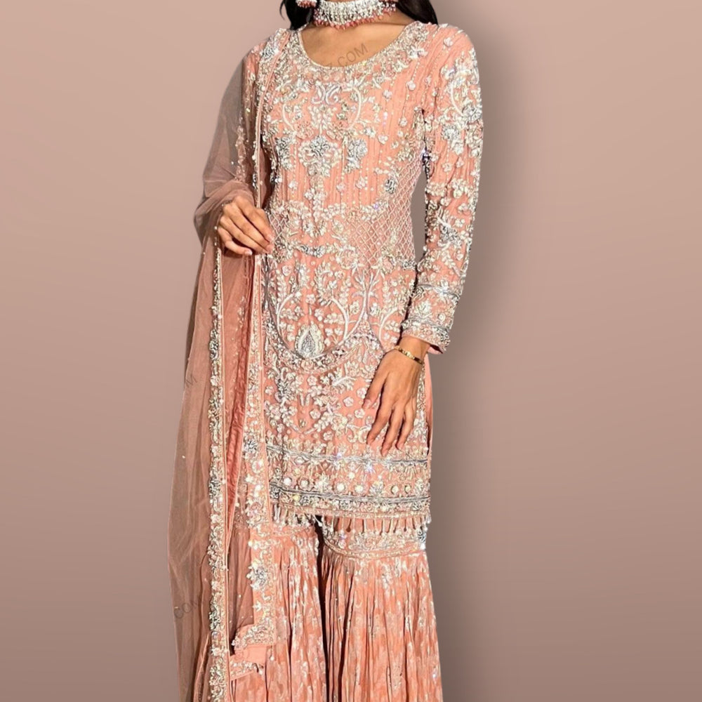 Woman wearing a peach embroidered traditional outfit with a matching dupatta on a beige background, with 'GK' branding.