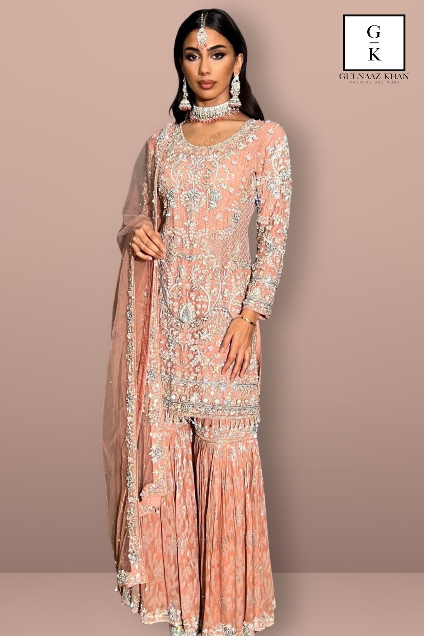 Woman wearing a peach embroidered traditional outfit with a matching dupatta on a beige background, with 'GK' branding.