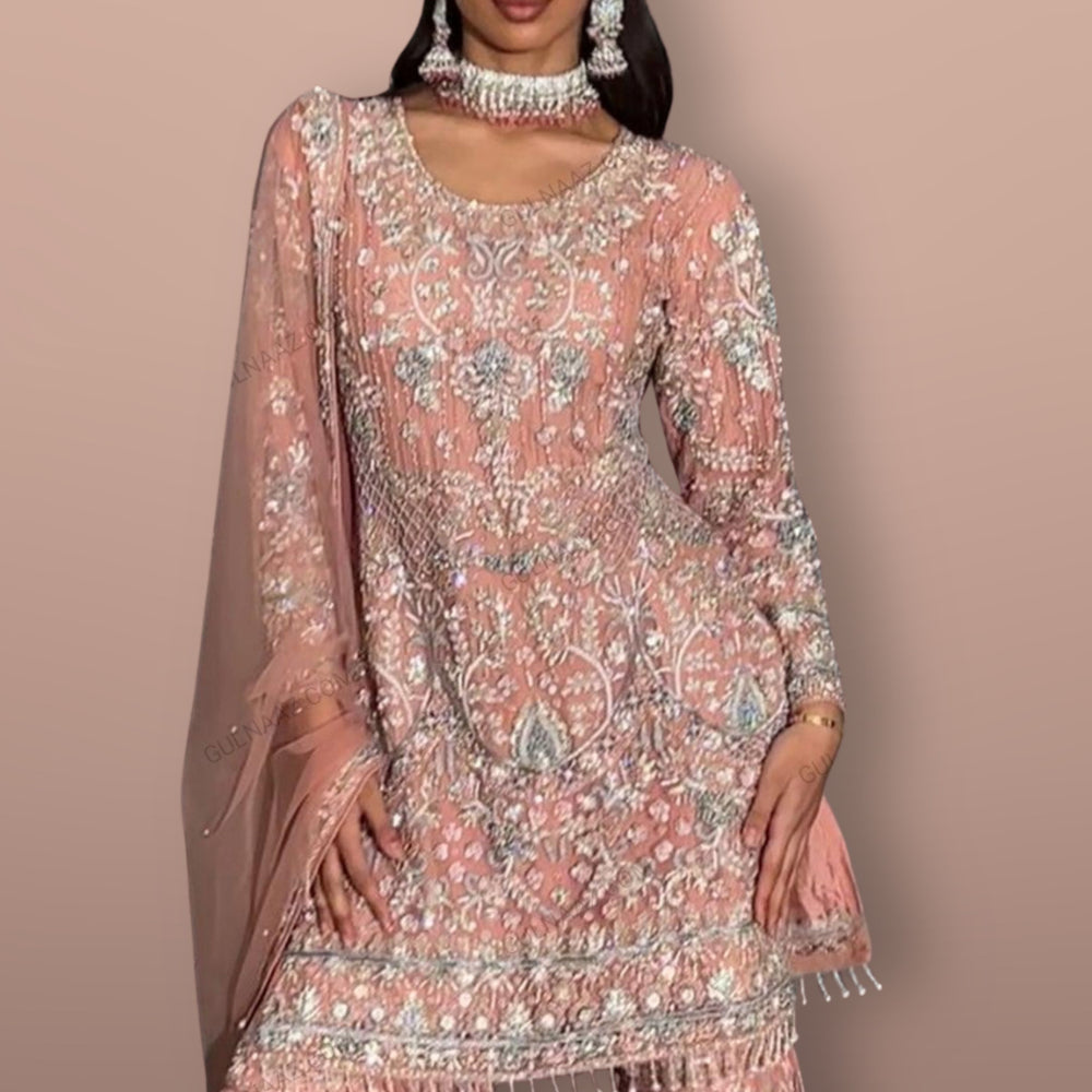 Woman wearing a pink embroidered traditional outfit with jewelry on a beige background, featuring the brand 'GK'.