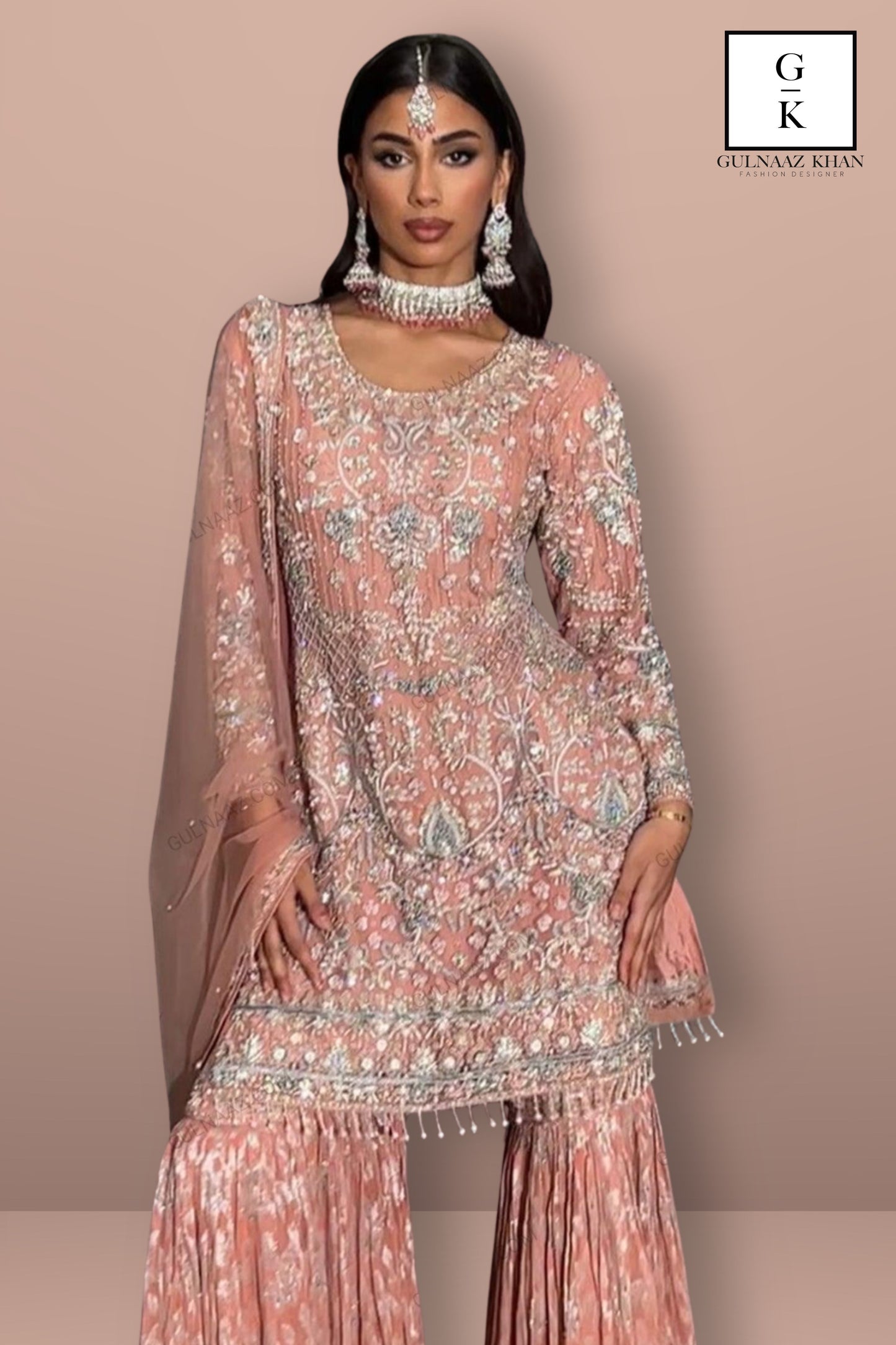Woman wearing a pink embroidered traditional outfit with jewelry on a beige background, featuring the brand 'GK'.