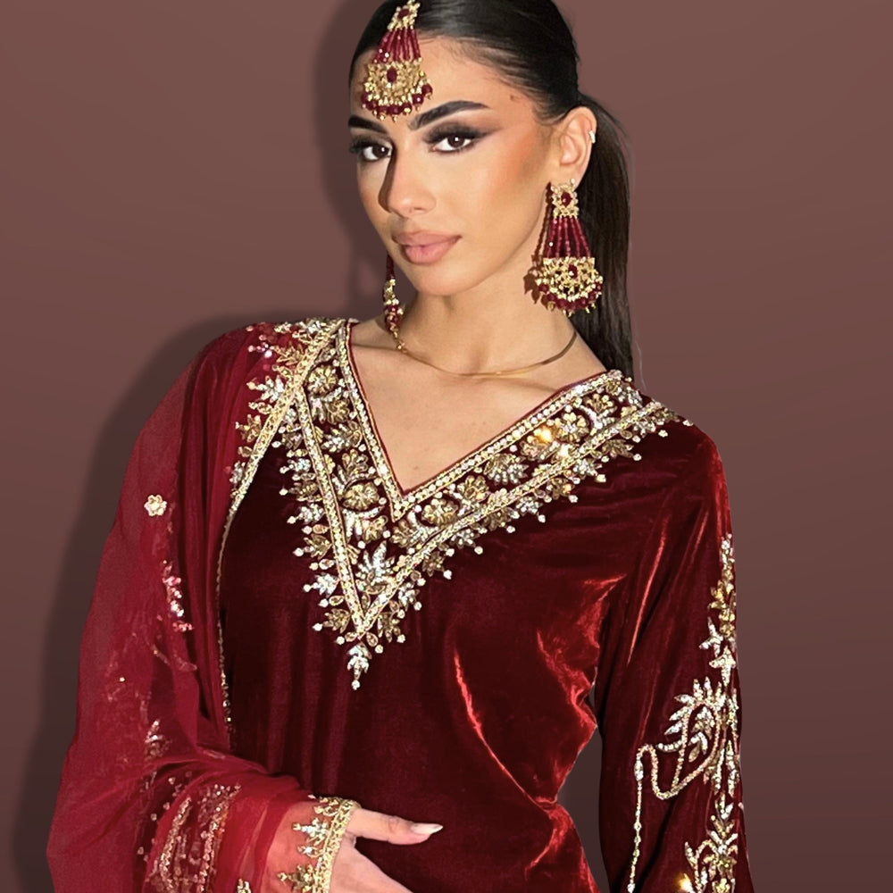 Woman wearing a red embroidered traditional outfit with gold details on a brown background